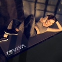Une femme réalisant un entraînement abdominal sur le tapis de protection de sol AsVIVA UM2 dans un studio sombre